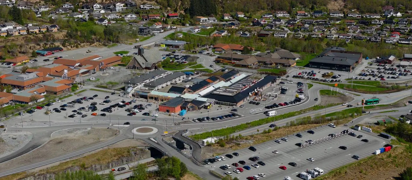 Luftfoto av Aksdal Senteret med parkeringsplasser, rundkjøring og boligområdene rundt