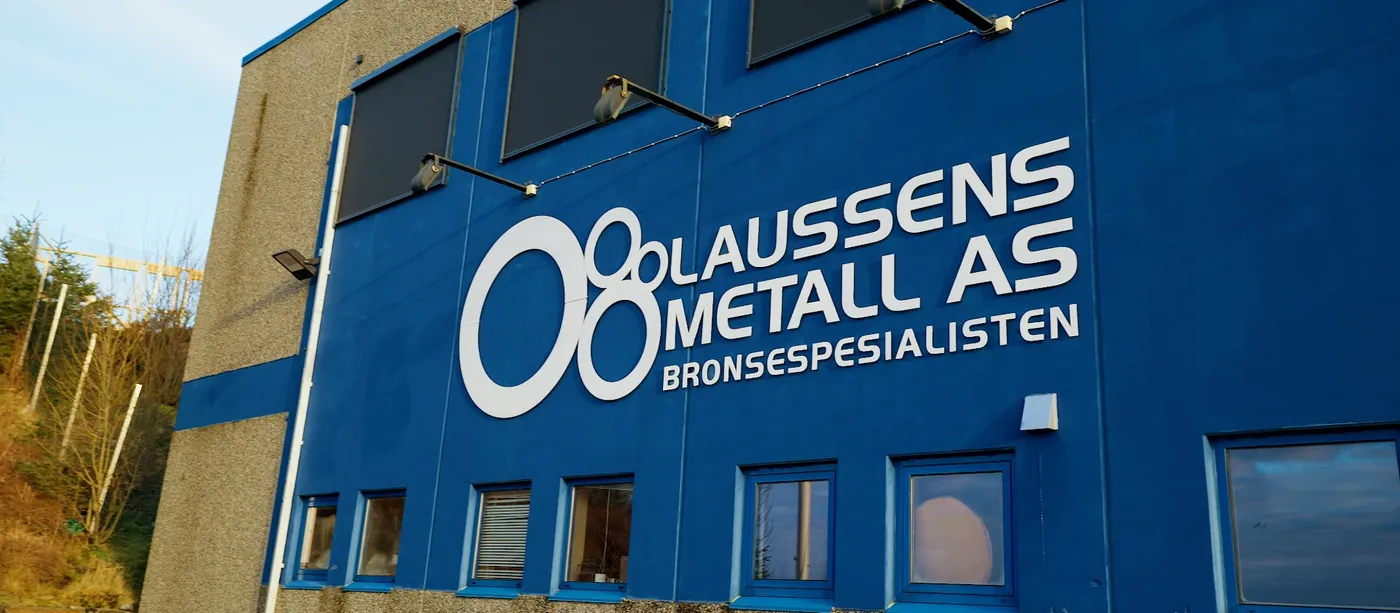 Bygningen til Olaussen Metall AS med bedriftens logo og navn på den blå fasaden